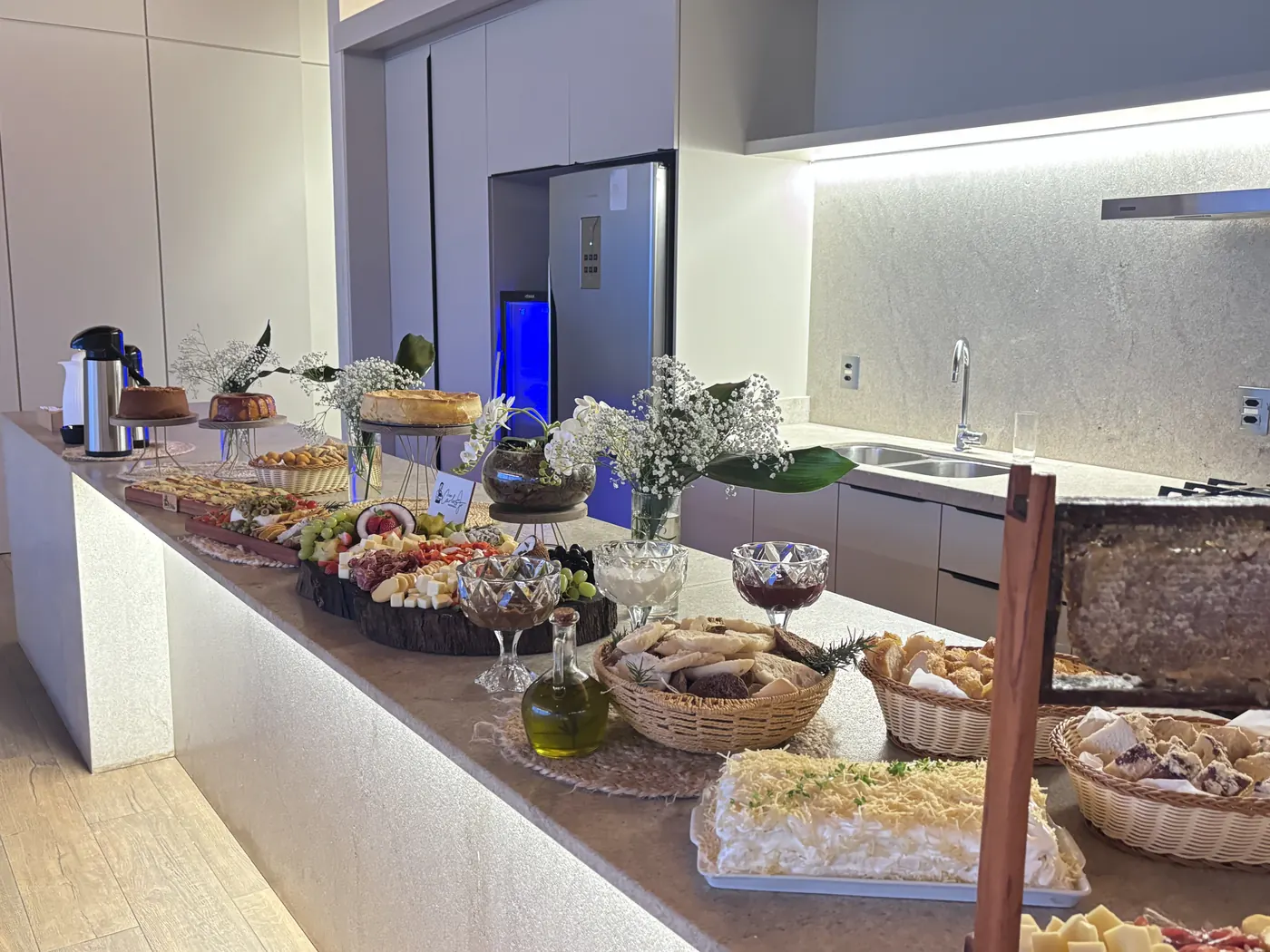 Bancada de coffee break com bolos, frios, pães e flores