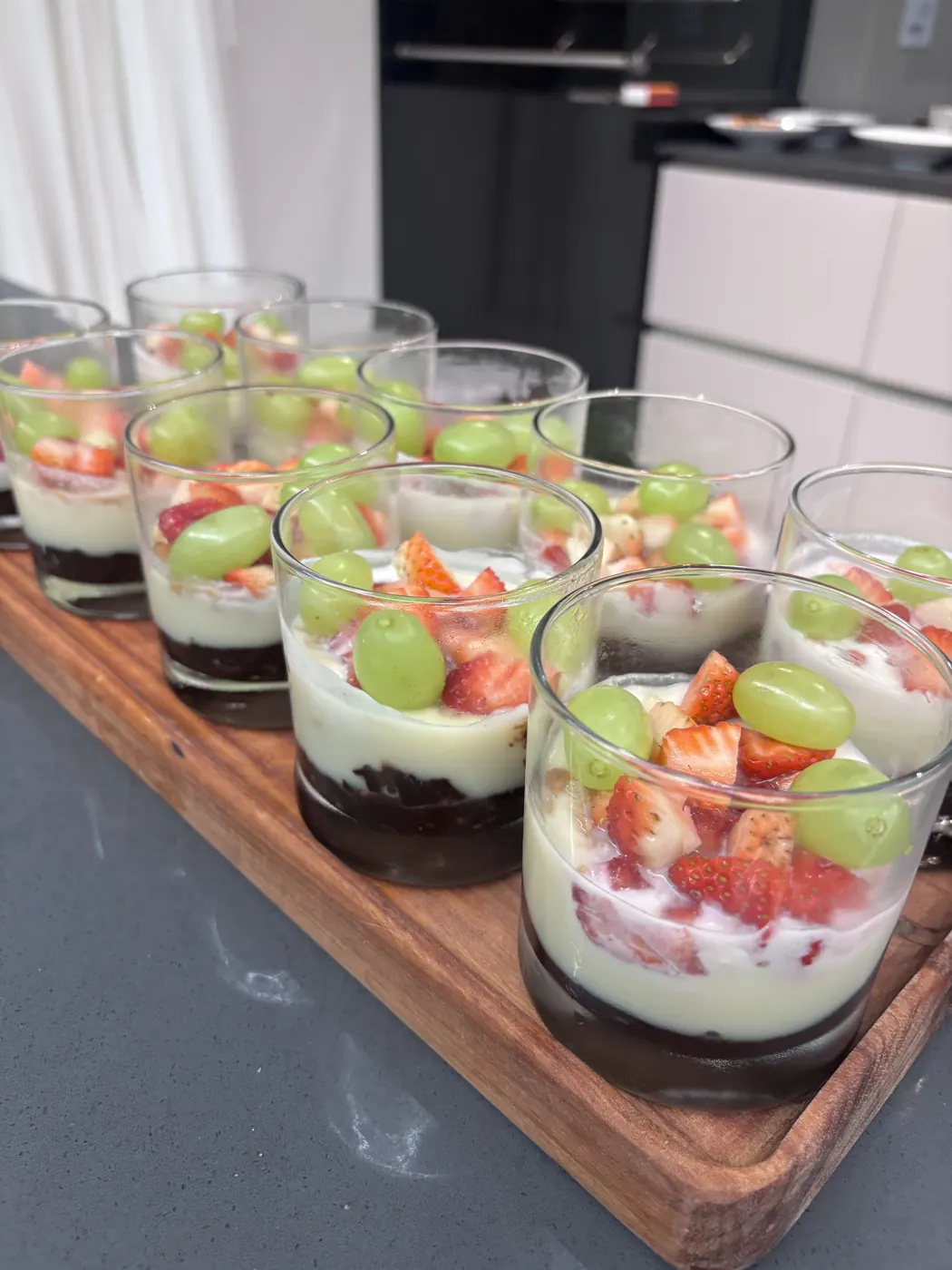 Verrines de creme com morangos e uvas sobre bandeja de madeira